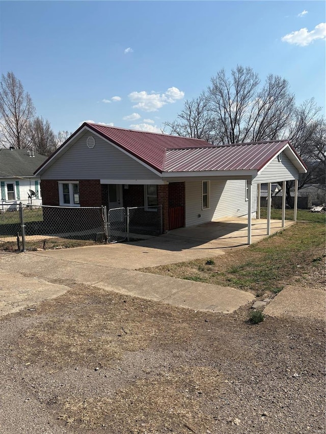 exterior space featuring fence, a carport, concrete driveway, brick siding, and metal roof