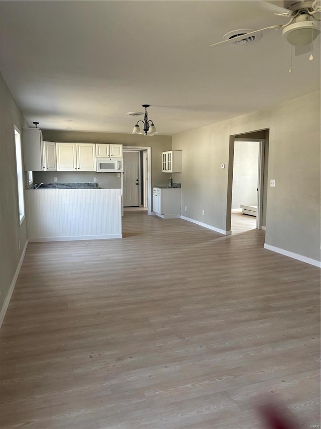 unfurnished living room with ceiling fan with notable chandelier, visible vents, baseboards, and light wood-type flooring