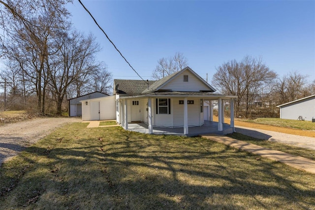 view of front of property with a front lawn, a porch, roof with shingles, an outdoor structure, and driveway