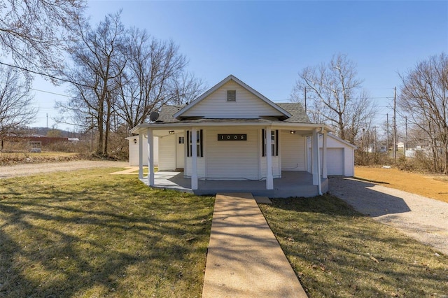 view of front of property featuring gravel driveway, covered porch, an outdoor structure, a front yard, and a garage