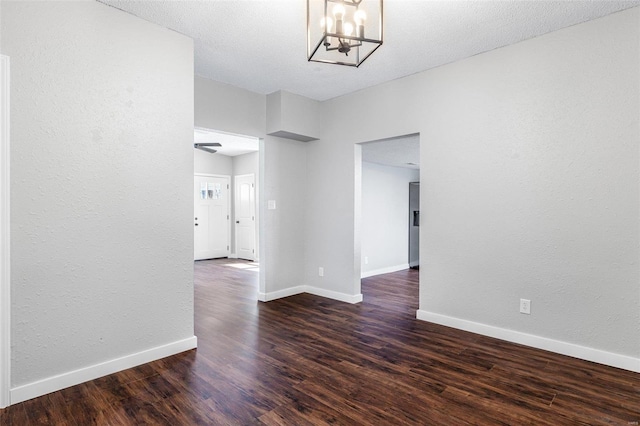 empty room with baseboards, a notable chandelier, and dark wood finished floors