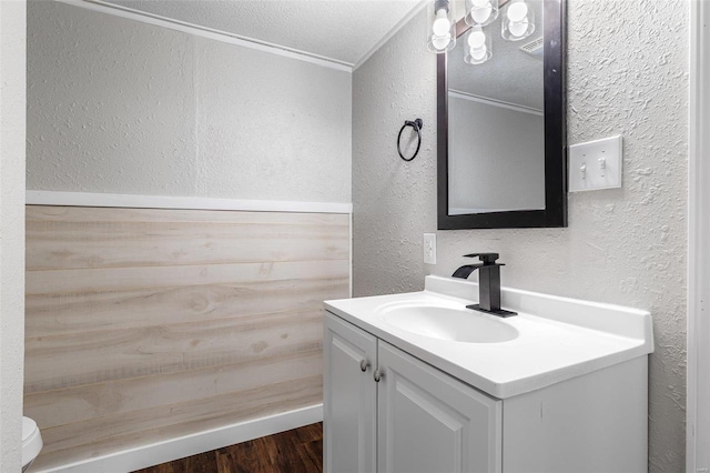 bathroom featuring toilet, vanity, a textured wall, wood finished floors, and a textured ceiling