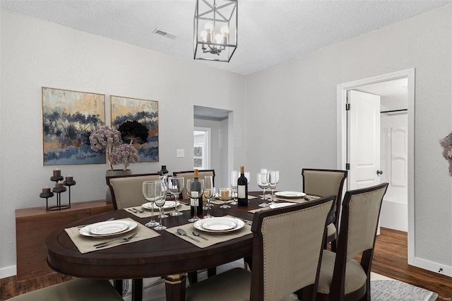 dining space with visible vents, baseboards, an inviting chandelier, wood finished floors, and a textured ceiling