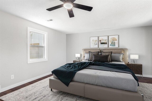 bedroom featuring visible vents, a textured ceiling, baseboards, and wood finished floors