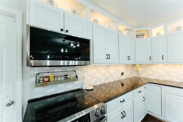 kitchen with dark stone countertops, stainless steel microwave, tasteful backsplash, white cabinetry, and range