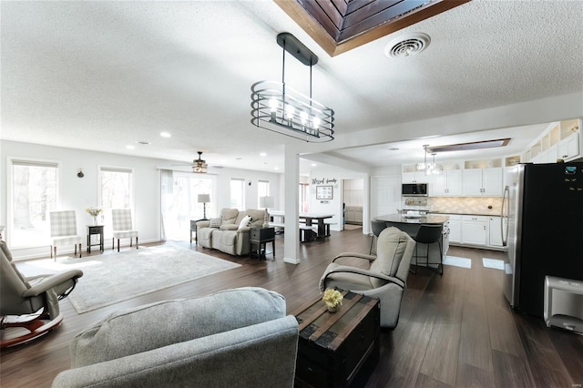 living area with visible vents, a textured ceiling, dark wood-style floors, and ceiling fan with notable chandelier