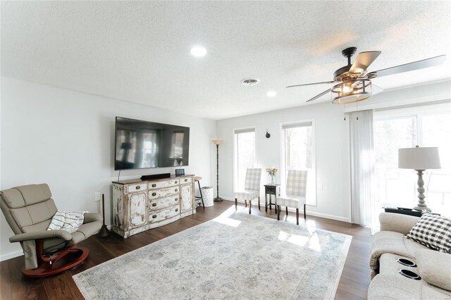 living room with a ceiling fan, baseboards, visible vents, dark wood-type flooring, and a textured ceiling