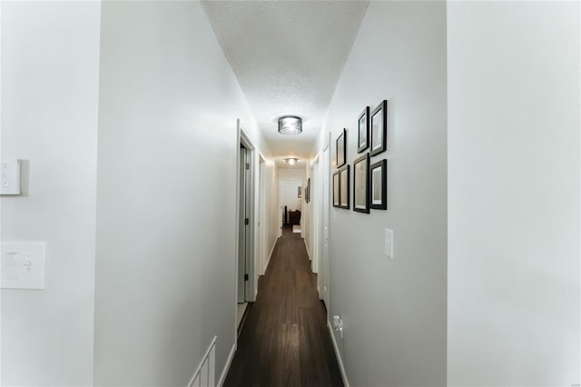 hall featuring visible vents, baseboards, a textured ceiling, and dark wood finished floors