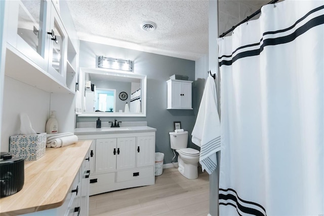 full bath with visible vents, toilet, a textured ceiling, wood finished floors, and vanity