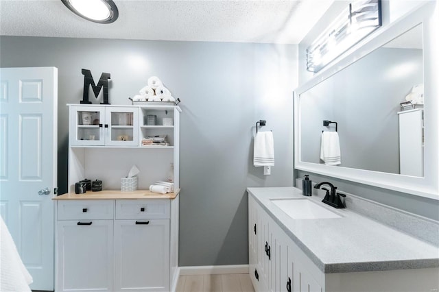 bathroom with vanity, wood finished floors, baseboards, and a textured ceiling