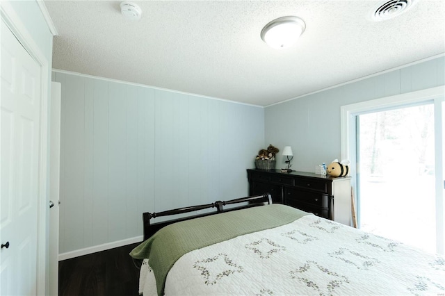 bedroom with a textured ceiling, dark wood-style floors, visible vents, and ornamental molding