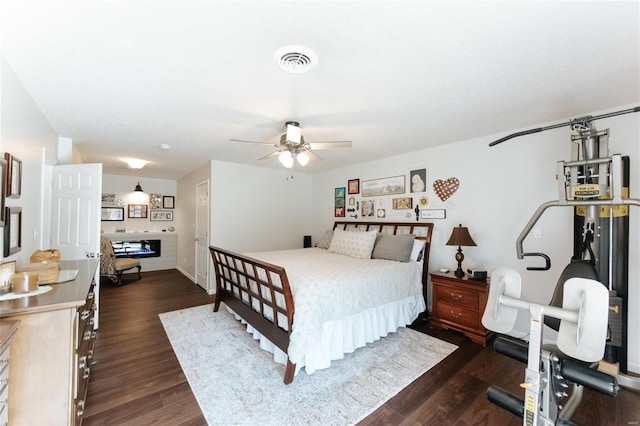 bedroom featuring visible vents, a fireplace, a ceiling fan, and dark wood-style flooring