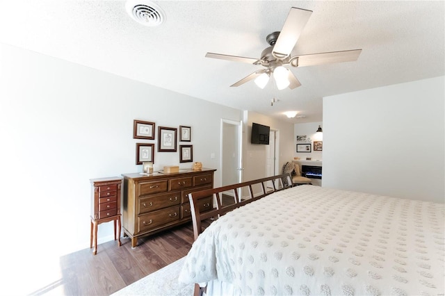 bedroom featuring ceiling fan, visible vents, a textured ceiling, and dark wood-style floors