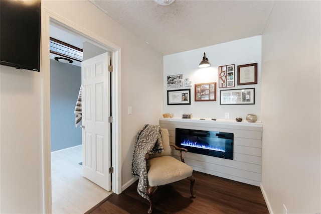 living area with baseboards, wood finished floors, a textured ceiling, and a glass covered fireplace