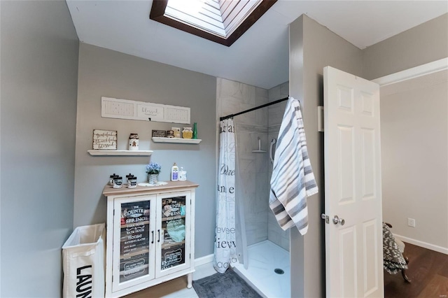 full bath with a shower stall, a skylight, wood finished floors, and baseboards