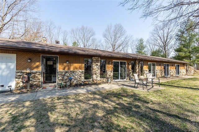 rear view of property featuring stone siding, a patio, a chimney, and a yard