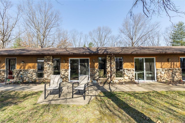 rear view of house featuring stone siding, a lawn, and a patio