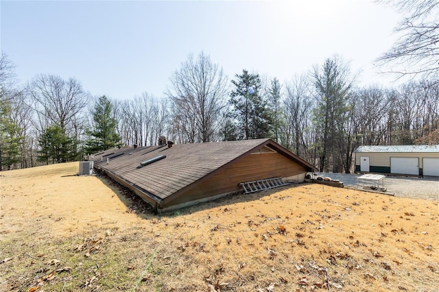 view of side of property with cooling unit, a garage, and roof with shingles