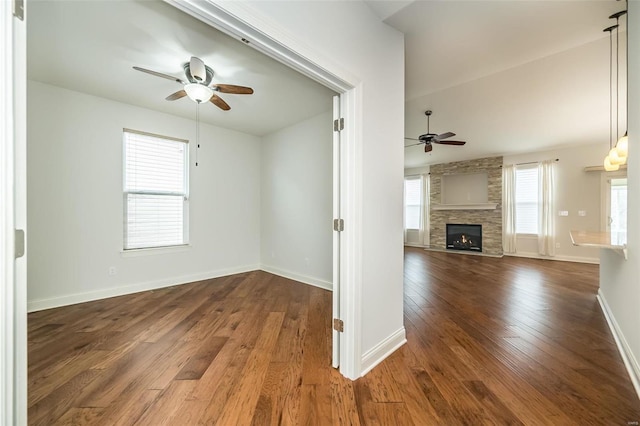 empty room featuring ceiling fan, baseboards, a large fireplace, and hardwood / wood-style floors