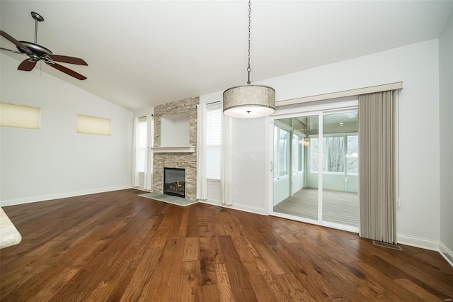 unfurnished living room with vaulted ceiling, a stone fireplace, baseboards, and wood finished floors