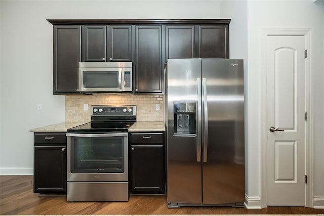 kitchen featuring light stone counters, decorative backsplash, stainless steel appliances, and wood finished floors