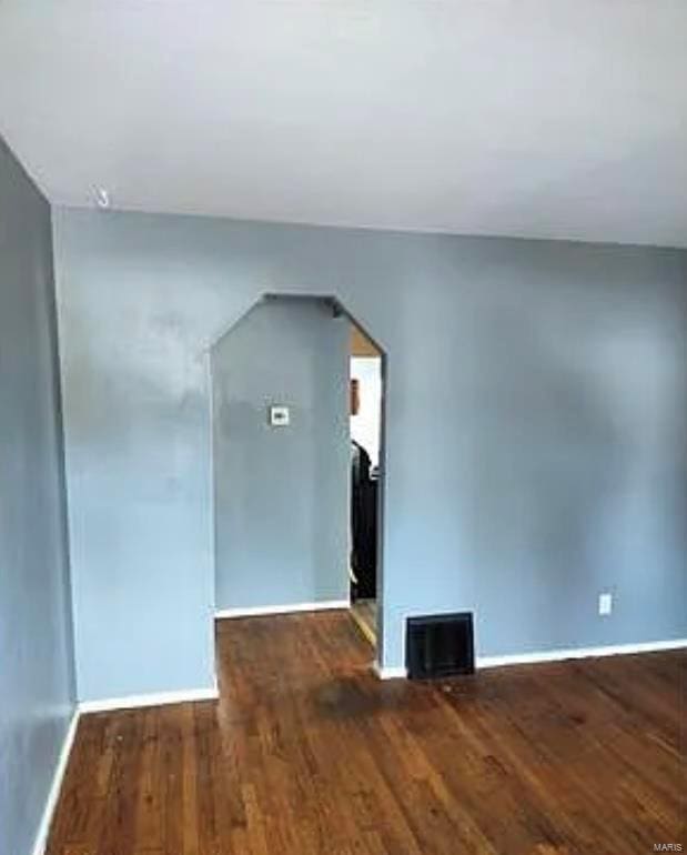 unfurnished room featuring visible vents, baseboards, arched walkways, and wood finished floors