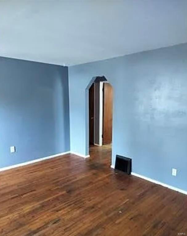 unfurnished room featuring arched walkways, visible vents, baseboards, and wood finished floors