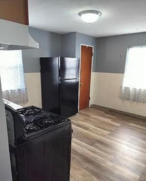 kitchen with light wood-style flooring, black appliances, range hood, and wainscoting