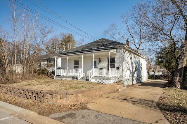 view of front of property with driveway, a porch, a chimney, and a shingled roof