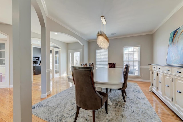 dining room with arched walkways, crown molding, light wood-type flooring, and baseboards