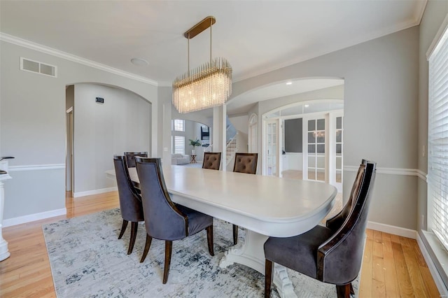 dining space with arched walkways, visible vents, light wood finished floors, and crown molding