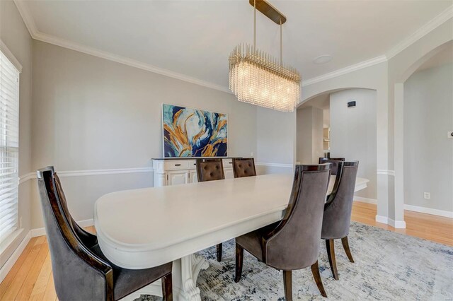 dining area with arched walkways, crown molding, and light wood-style floors