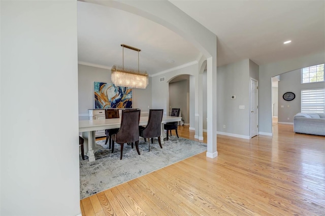 dining space featuring an inviting chandelier, crown molding, arched walkways, and light wood-type flooring