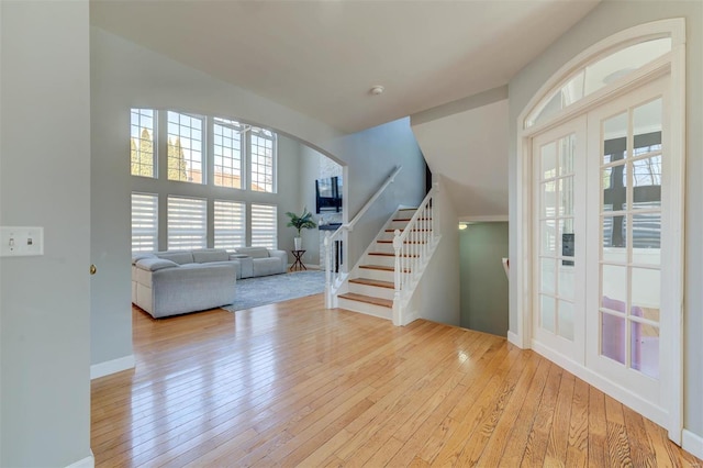 entryway with stairway, arched walkways, baseboards, and light wood-style flooring