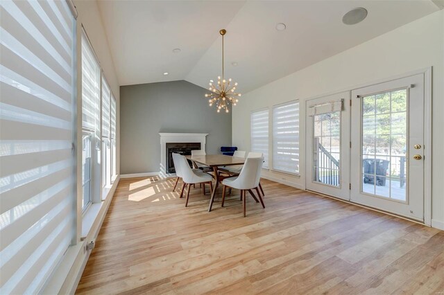 dining area featuring light wood finished floors, a chandelier, a fireplace, and vaulted ceiling