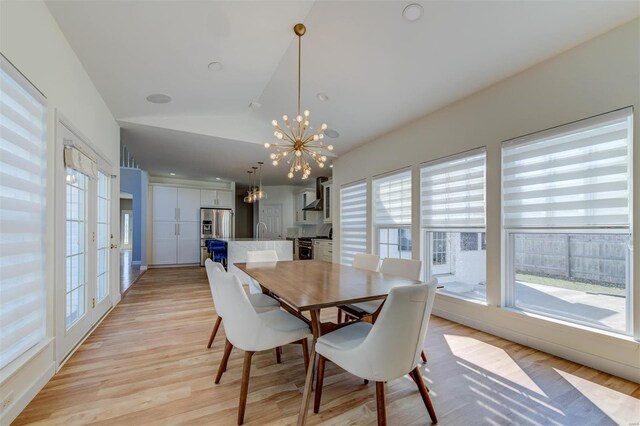 dining space featuring a healthy amount of sunlight, light wood-style flooring, an inviting chandelier, and vaulted ceiling