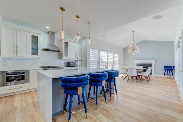 kitchen featuring light wood-style flooring, wall chimney exhaust hood, white cabinets, stainless steel oven, and vaulted ceiling