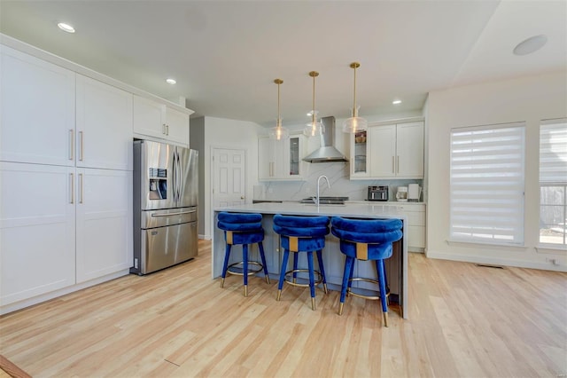 kitchen with a breakfast bar area, light countertops, light wood-style floors, stainless steel refrigerator with ice dispenser, and wall chimney exhaust hood