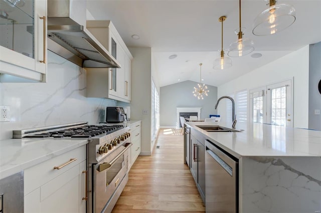 kitchen featuring light wood-style flooring, a sink, stainless steel appliances, wall chimney exhaust hood, and lofted ceiling