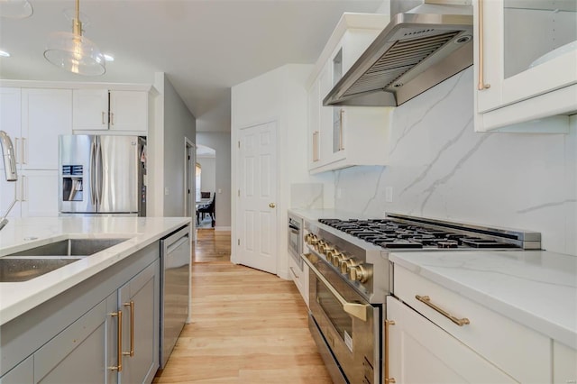 kitchen featuring a sink, decorative backsplash, light wood-style floors, appliances with stainless steel finishes, and wall chimney exhaust hood