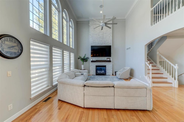 living room with visible vents, ornamental molding, a high ceiling, a stone fireplace, and baseboards