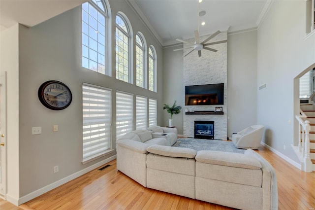 living area featuring visible vents, a fireplace, stairs, light wood-style floors, and crown molding