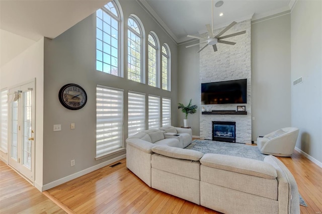 living room with visible vents, ornamental molding, hardwood / wood-style floors, a high ceiling, and a stone fireplace