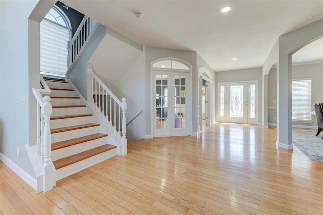 entryway with stairway, light wood-style flooring, baseboards, and arched walkways