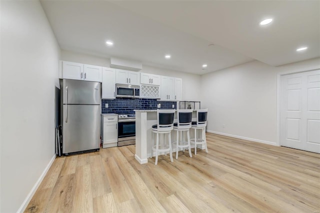 kitchen with light wood-type flooring, a breakfast bar, appliances with stainless steel finishes, white cabinets, and decorative backsplash