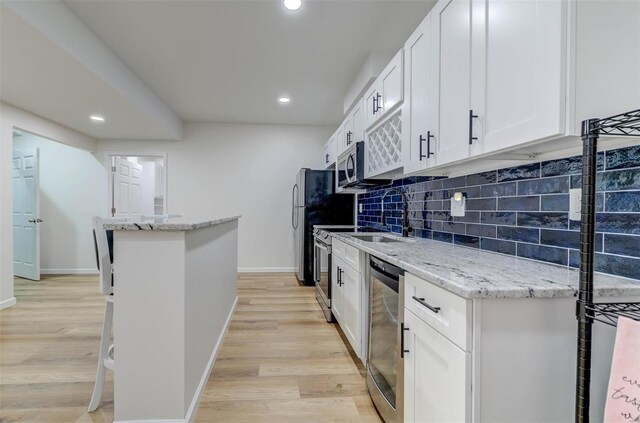 kitchen featuring tasteful backsplash, a kitchen island, white cabinetry, appliances with stainless steel finishes, and light wood finished floors