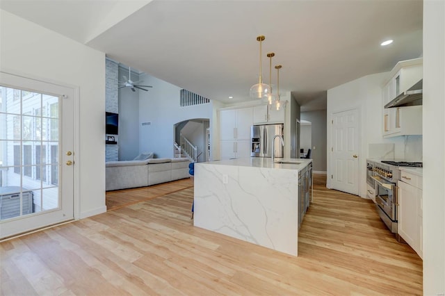 kitchen with light wood-style flooring, ceiling fan, a sink, appliances with stainless steel finishes, and wall chimney range hood