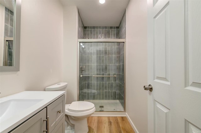 bathroom with a stall shower, toilet, wood finished floors, and vanity