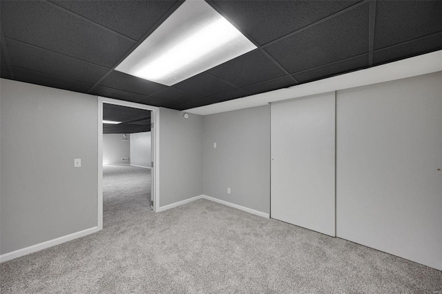 finished below grade area featuring a paneled ceiling, carpet floors, and baseboards