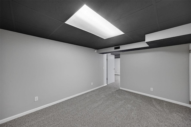 finished basement featuring visible vents, baseboards, a paneled ceiling, and carpet